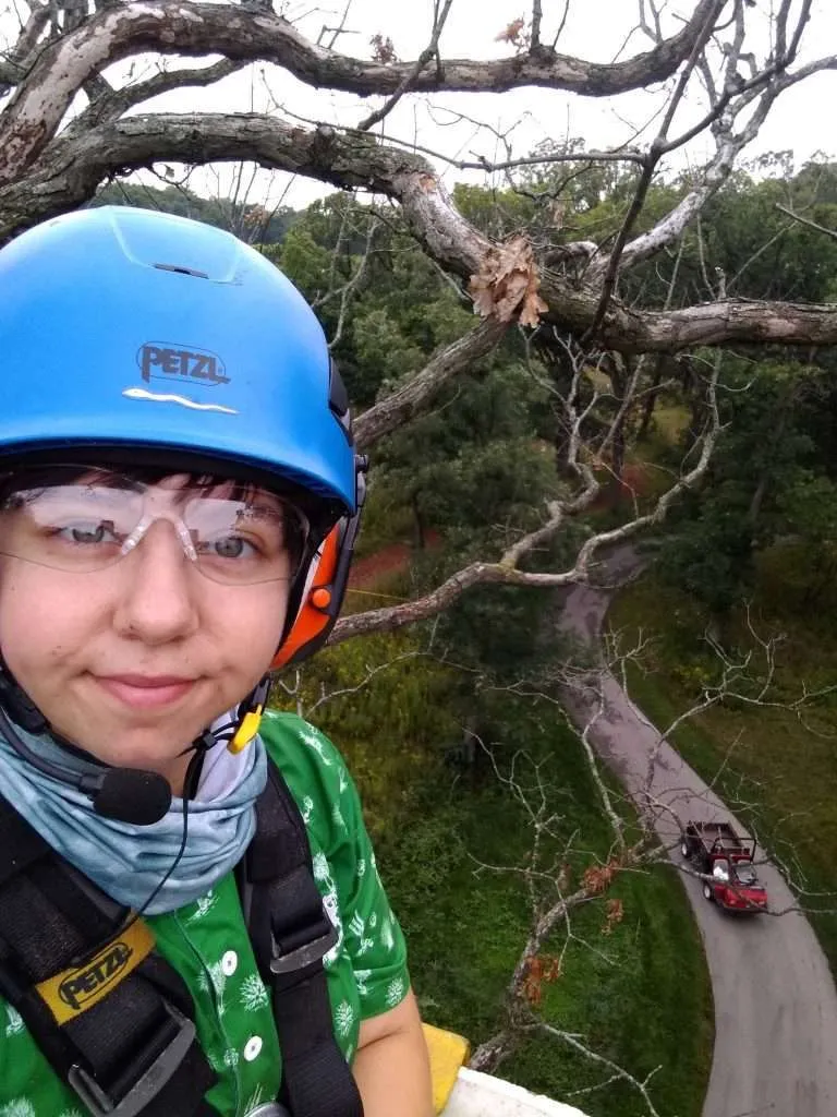 A young person wearing a helmet and glasses while perched on a tree branch.