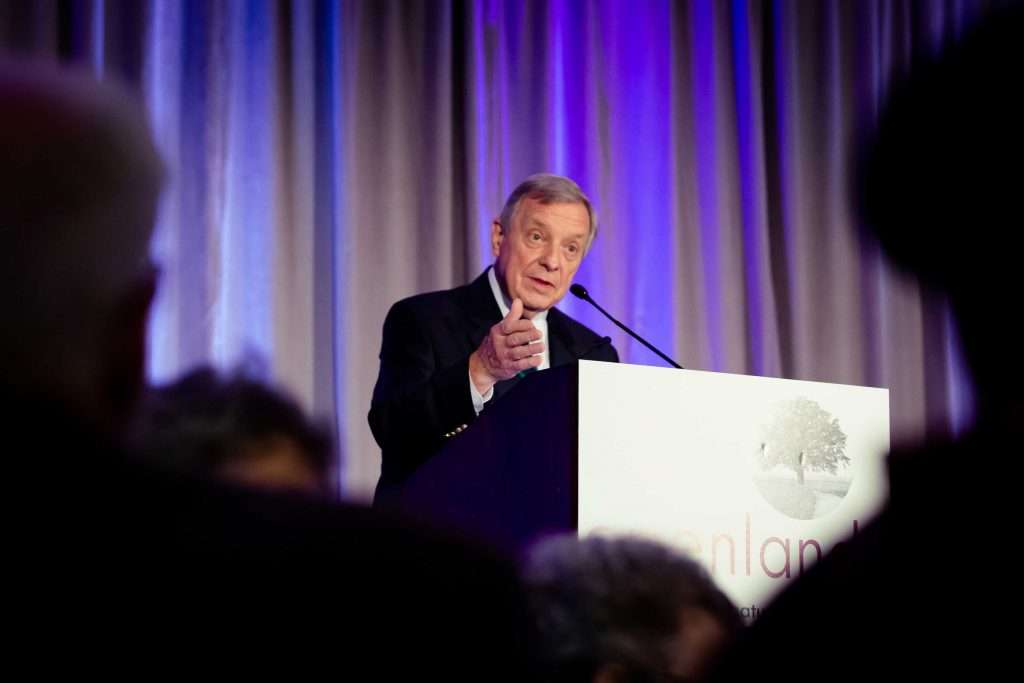 A man in a suit delivering a speech at a podium, addressing an audience with confidence and authority. (Senator Durbin)