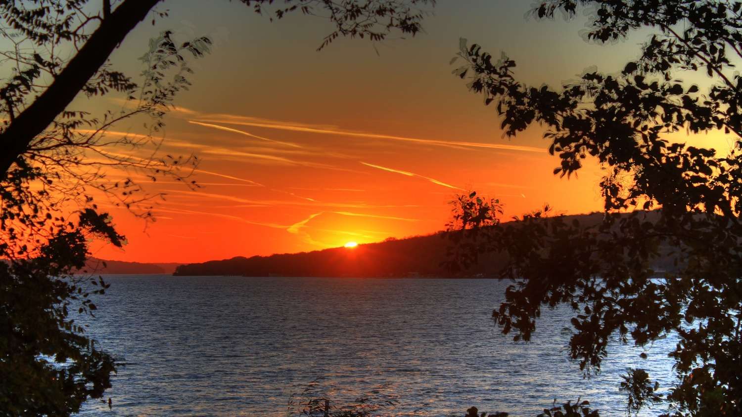 a sunset over a lake with trees silhouetted in the foreground