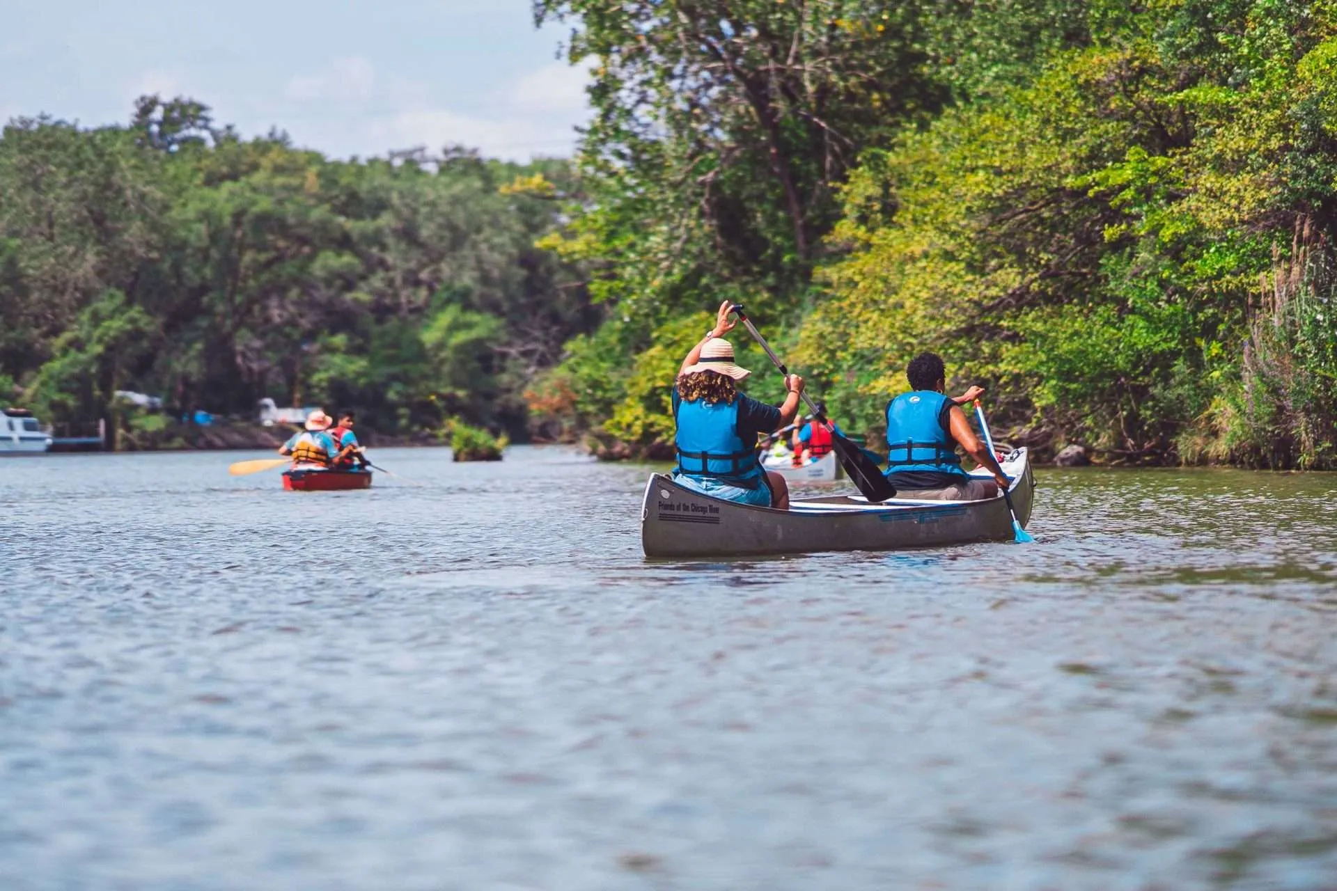 Kayakers on a river surrounded by green trees on a sunny day.