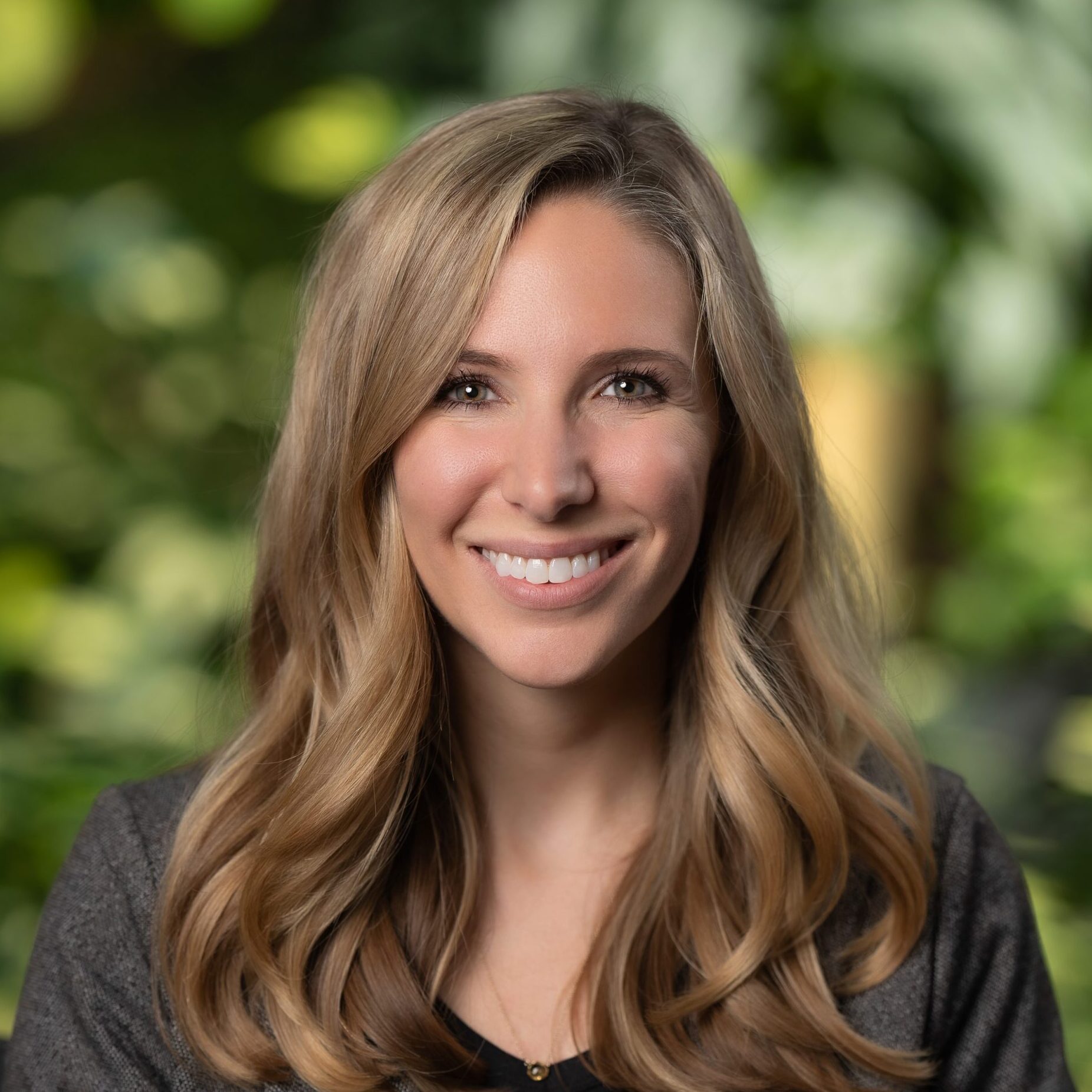 A woman wearing a blazer and a blurry nature background for a Openlands headshot