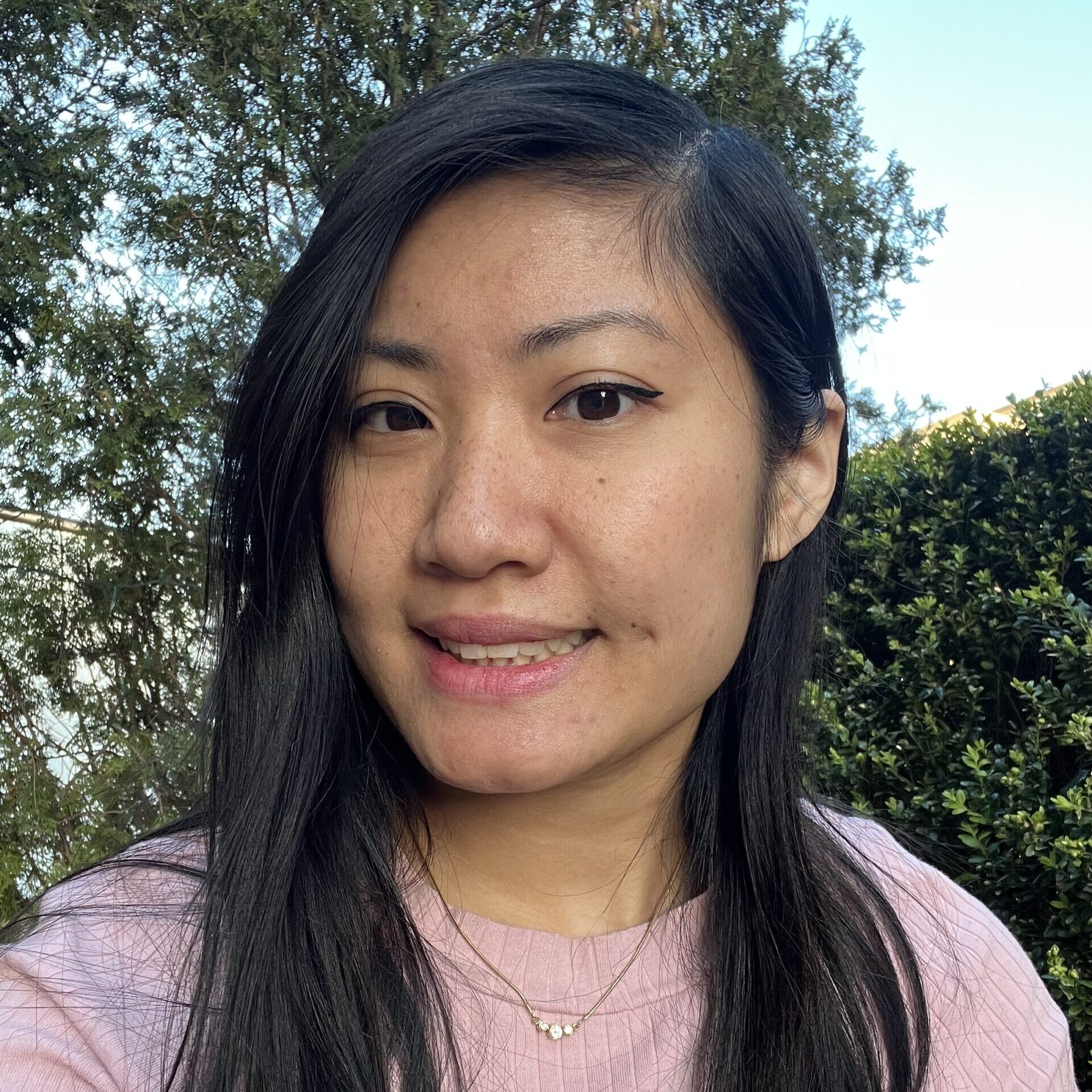 A woman with a pink shirt and a leafy hedge in the background