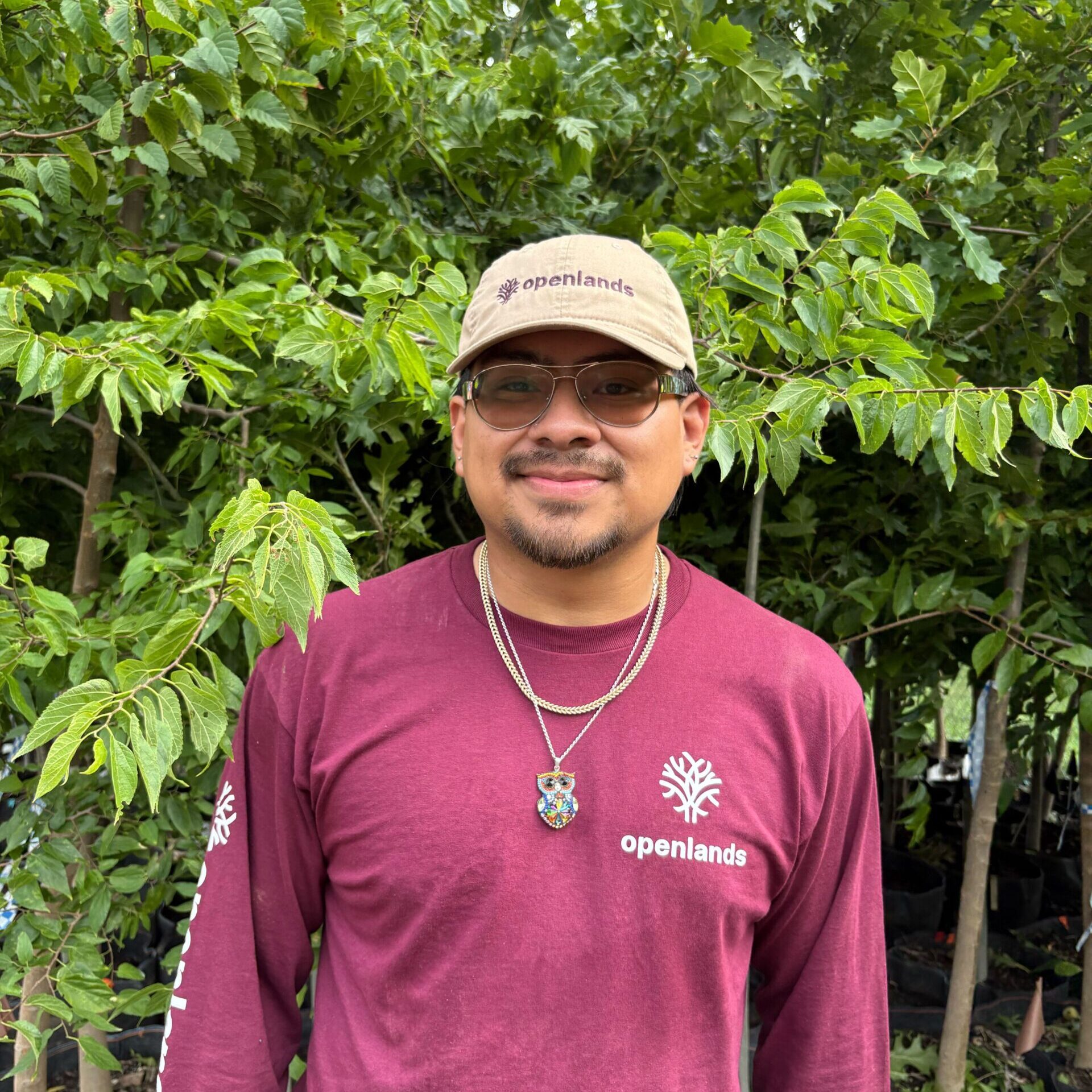A guy with an Openlands branded burgundy shirt, a gray hat and a nature background.