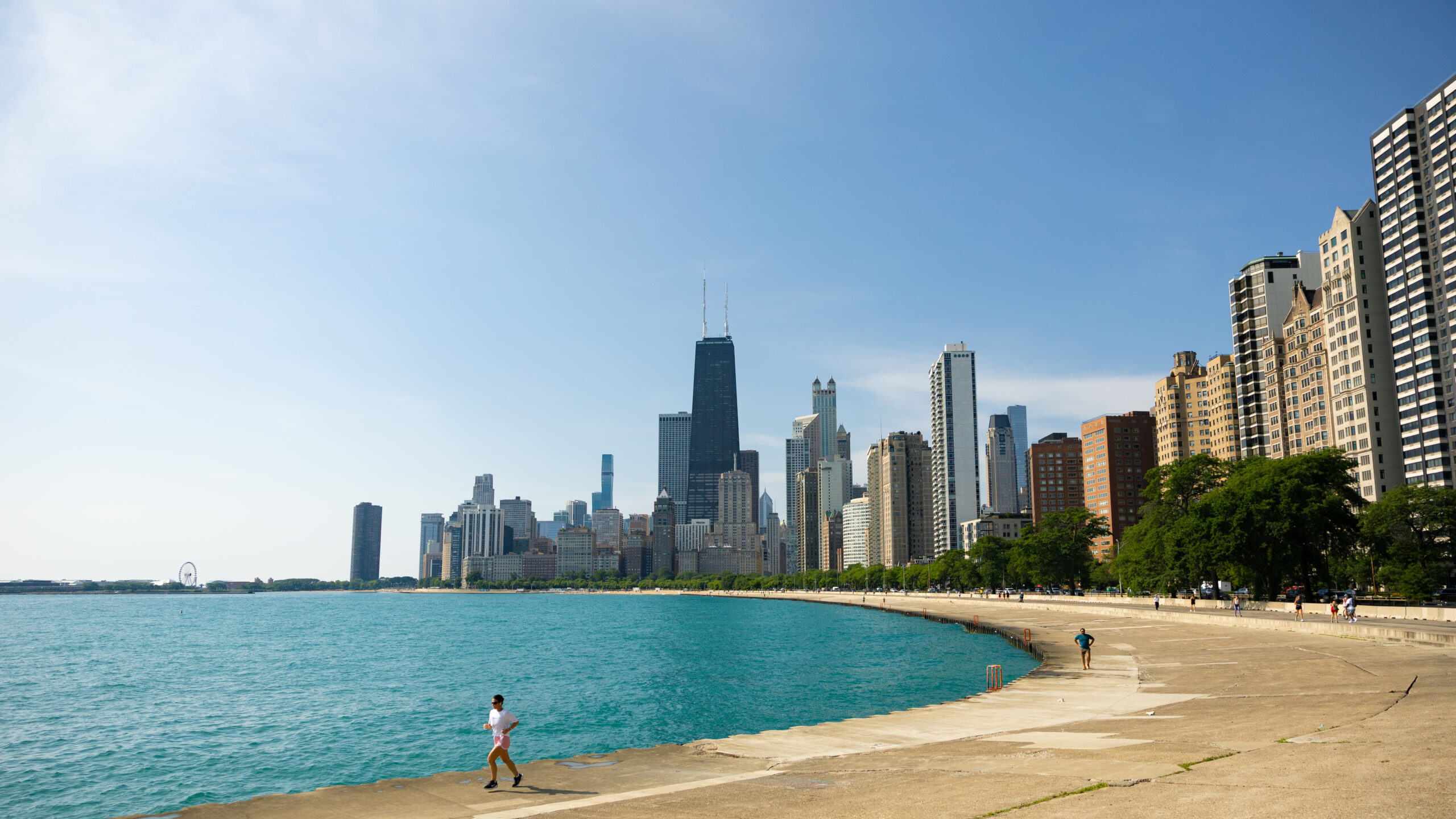 Person running on white shirt along Lake Michigan with skyscrapers of Chicago in background.