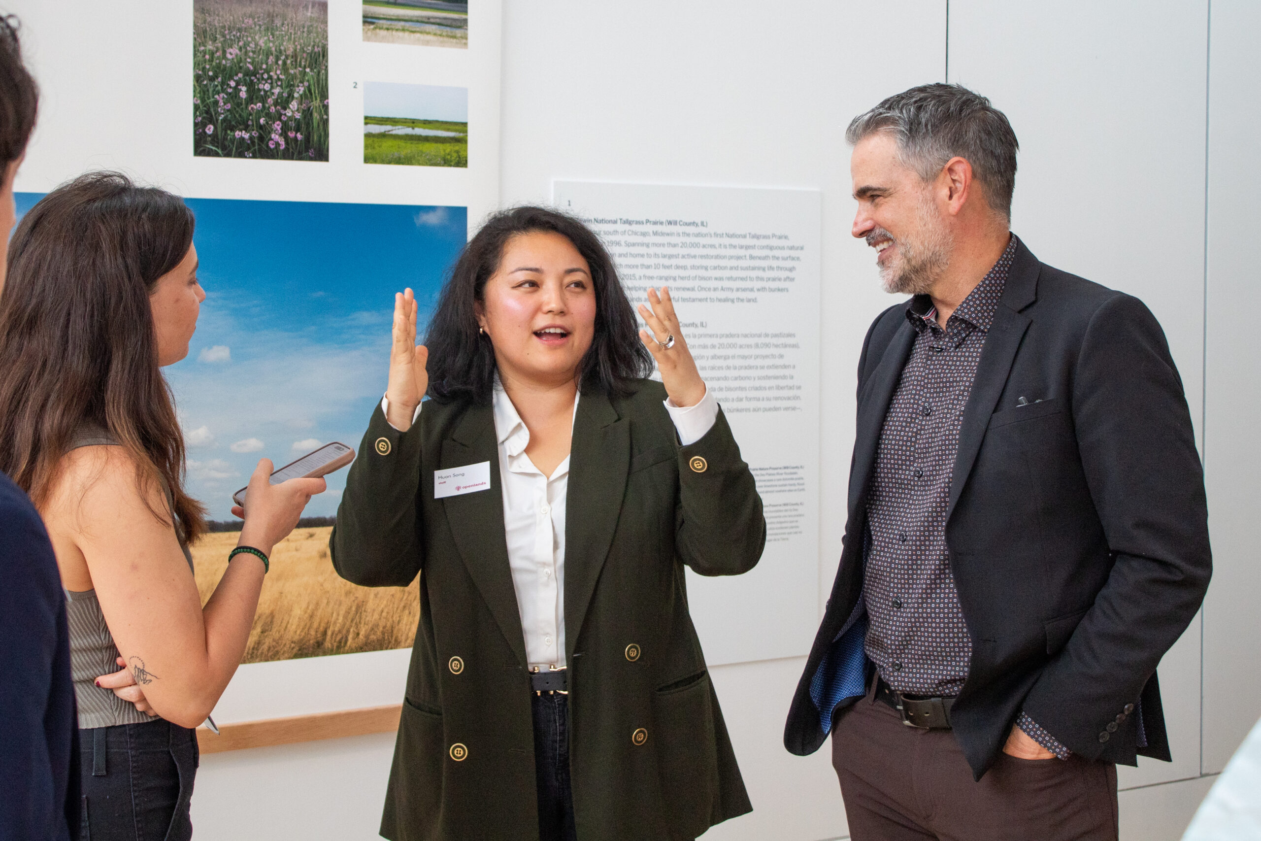 A woman in a green blazer presents on an exhibit with photos of prairie in the background.