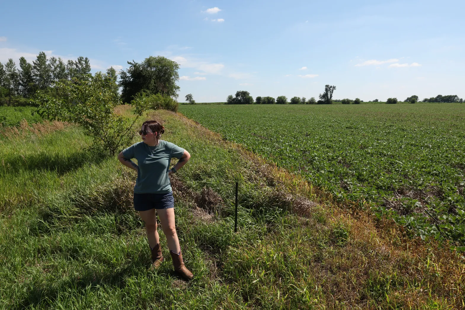 Woman stands on edge of her property which borders farmland.